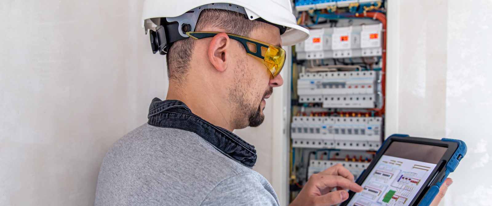 Eletricista verificando um quadro de disjuntores com tablet